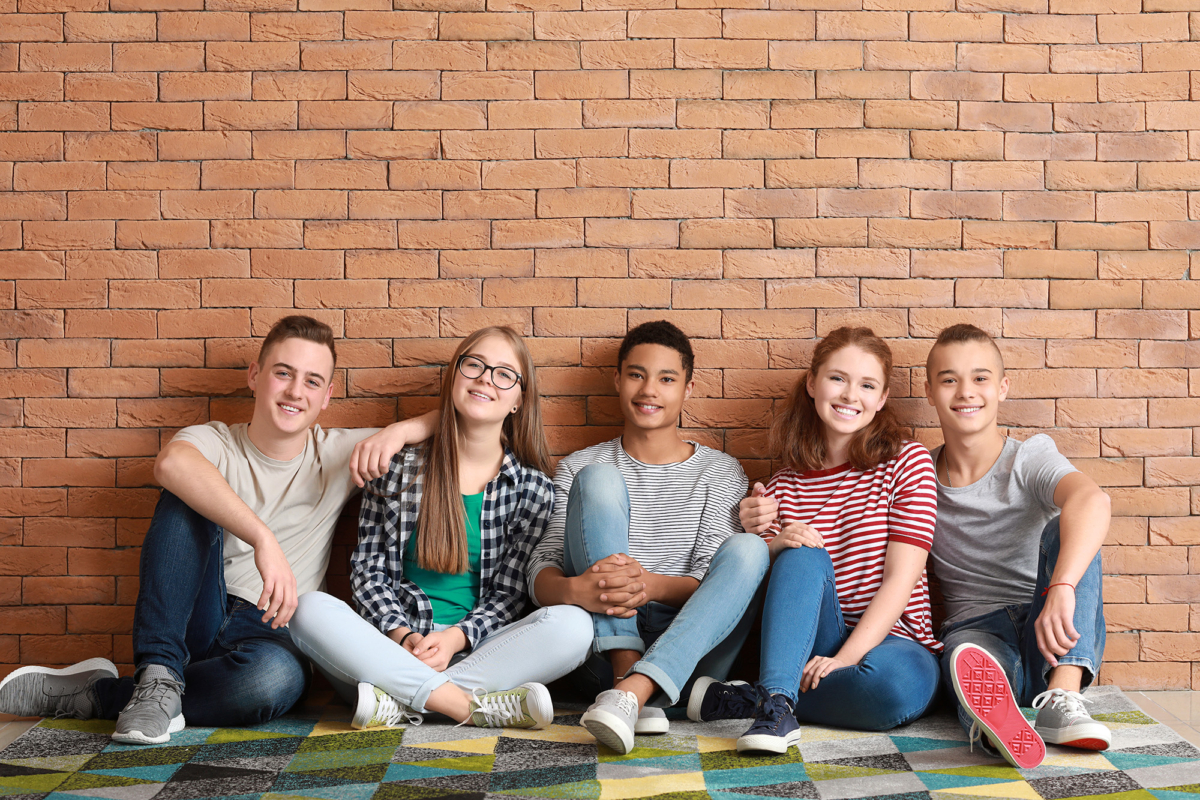 Group of teenagers sitting on floor near brick wall